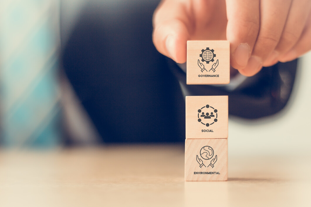 ESG concept of environmental, social and governance. Sustainable and ethical business. Businessman holds vertical wooden cubes with ESG icon on beautiful white background. Copy space.